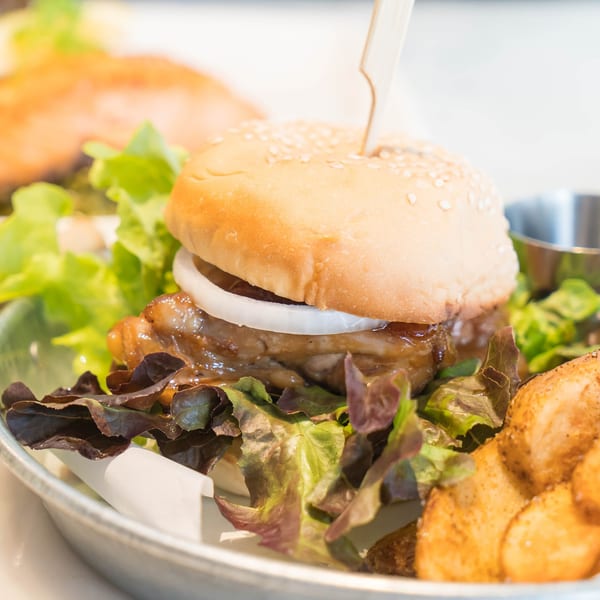 A close-up of a chicken burger with onions, lettuce, and a side of potato wedges.