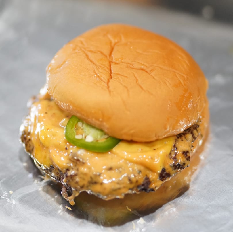 Cheeseburger with melted cheese, special sauce, and sliced jalapeños on a bun.