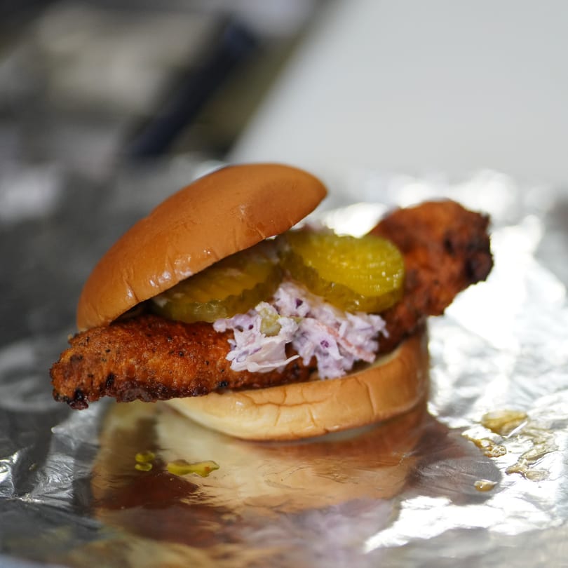Crispy fried chicken sandwich with pickles and coleslaw on a bun, resting on foil.