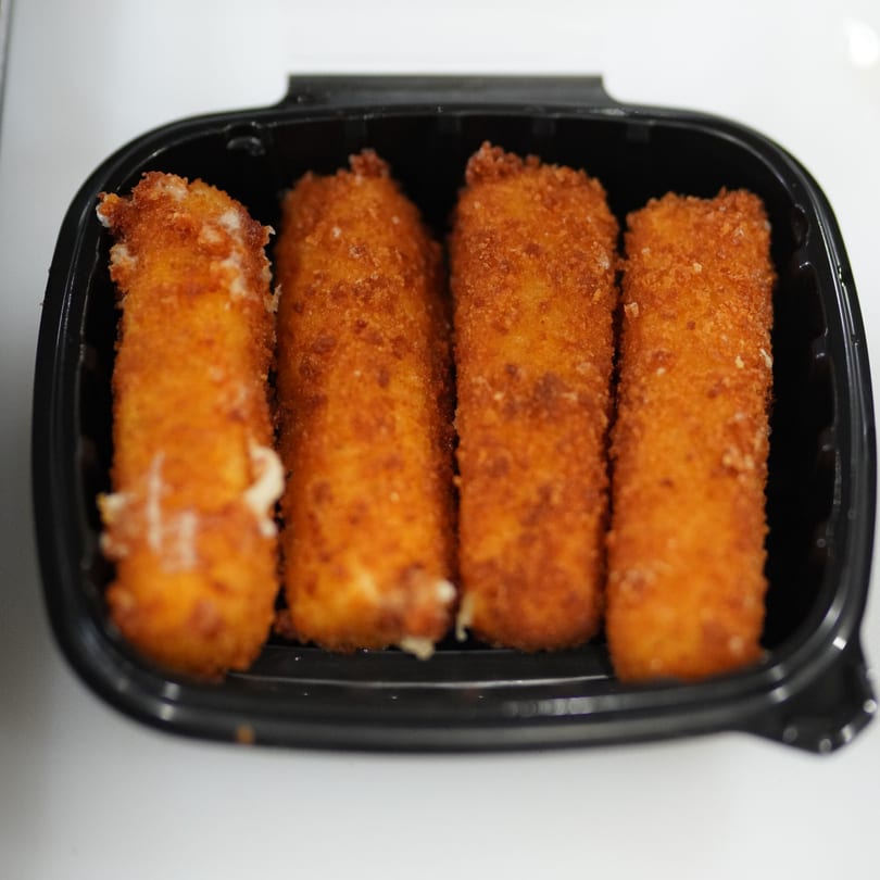 Four golden-brown mozzarella sticks, some with melted cheese peeking out, in a black plastic container.